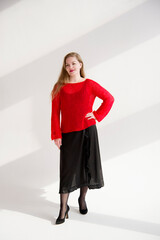 young blonde smiling beautiful lady in red handmade sweater and black skirt and black flower on the neck posing in white studio
