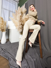 Smiling young woman sitting against beige background. Female resting at modern living room with home decor. Advertising concept of casual clothes