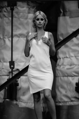 Young woman with long blonde hair, wearing a stylish white dress, poses confidently with a soft smile, showcasing elegance and beauty in a monochrome portrait