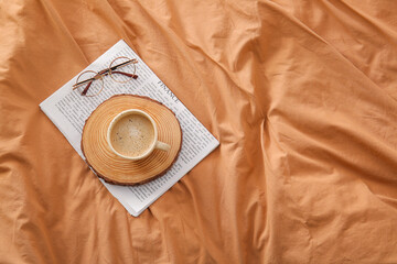 Tray with cup of coffee, newspaper and eyeglasses on beige bed sheets