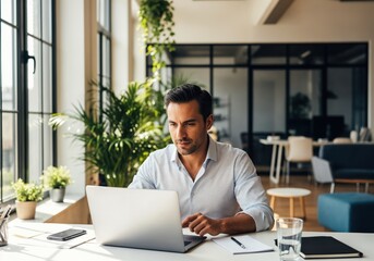 Obraz premium Focused businessman working on laptop in stylish modern office with greenery