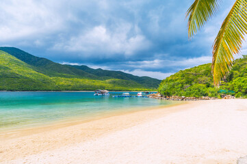 white sandy beach on tropical island in a bay by the sea in summer. Luxury exotic resort with beach and palm trees for relaxing in traveling in Asia. Landscape panorama with a view of coast by ocean