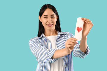 Young woman holding menstrual pad with heart on blue background