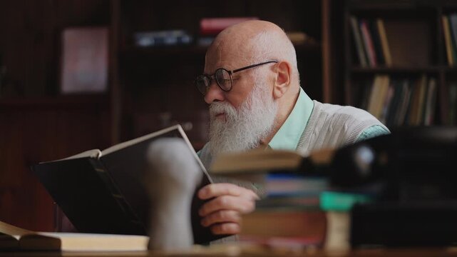 Concentrated elderly scientist reading a book with interest, doing research