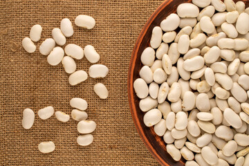 White uncooked beans on jute cloth, macro, top view.