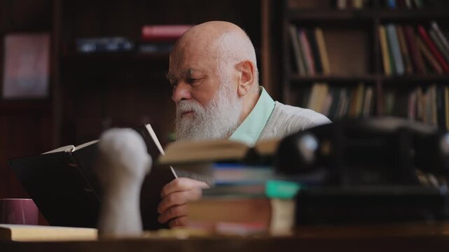 Focused senior teacher reading a book in library, preparing for his lesson