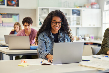 Happy smiling african american girl using laptop in class