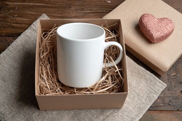 Gift box with a blank white ceramic mug and straw filler, next to a glittery heart