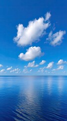 Obraz premium Vast Azure Ocean Meets Bright Blue Sky with Fluffy White Clouds and Sunlit Ripples Reflecting Sunlight in a Serene Coastal Landscape