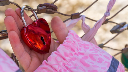 Child holding a shiny red heart padlock at the Makartsteg love lock bridge, Salzburg