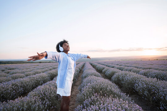 Happy woman with arms outstretched wearing wireless headphones in lavender field