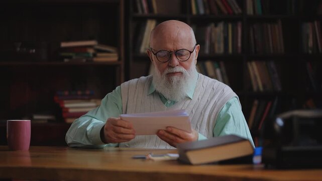 Elderly man in eyeglasses sorting mail in his study, checking monthly bills