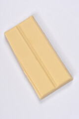 A portion of white chocolate with two segments is positioned at an angle on a light grey background, sloping up to the left