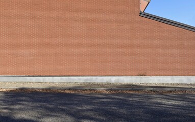High brick wall facade with roof and sky on the right. Concrete sidewalk and an asphalt street in front. Urban background for copy space