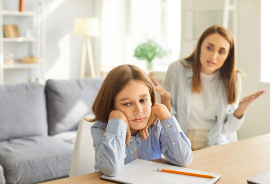 Upset emotional mother scolding her preteen son in attempt to resolve conflict. Frustrated boy sitting at desk, avoiding eye contact and refusing to discuss his emotions or school related issues.