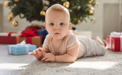 Happy small baby, first Christmas eve child on warm carpet near decorated festive tree, present...