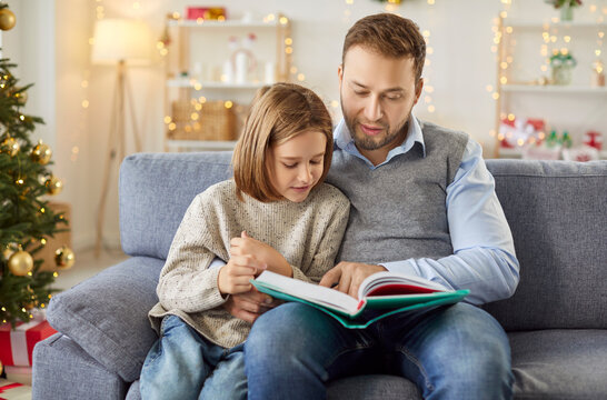 Father and son reading a book together at home during Christmas or New Year, creating a bonding experience. Shared leisure time fosters closeness, nurturing family warmth during the holiday season.