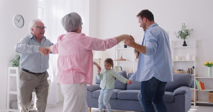 Happy family having fun together. Parents, grandparents and children having a party at home. Mother, father, grandmother, grandfather and kids dance in a circle, then clap hands and give high fives