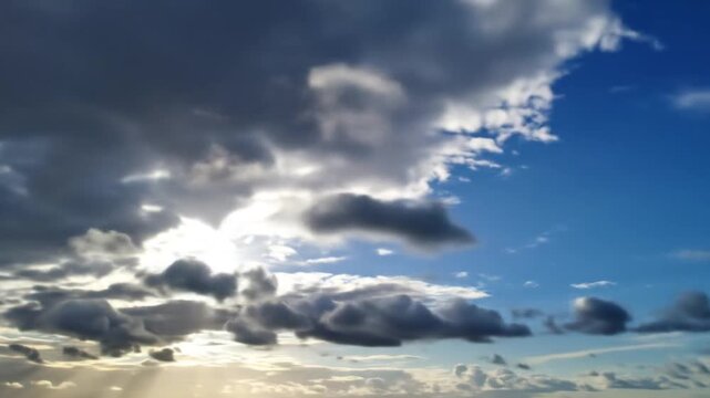 A sky view of puffy, dark clouds with bright patches of sunlight and a blue sky peeking