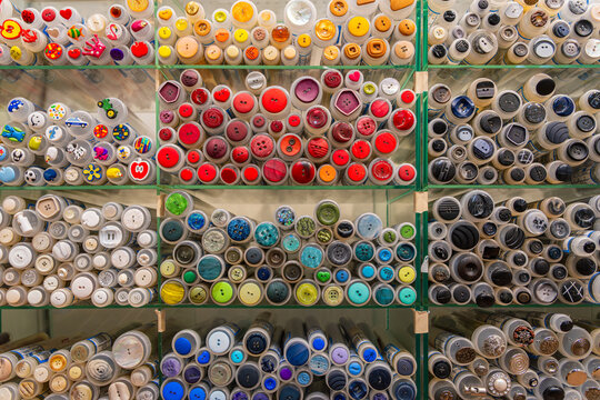 Colorful buttons in transparent tubes, neatly sorted by color and shape, create a vibrant pattern on a shop wall