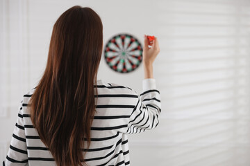Woman with dart aiming at dartboard indoors, back view. Space for text