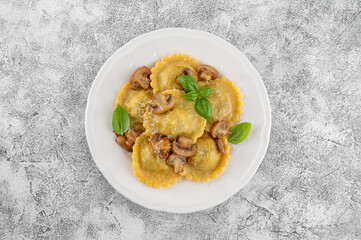 Tradition homemade Italian ravioli pasta with ricotta, mushrooms and parmesan cheese in a white plate on a concrete background. Top view.