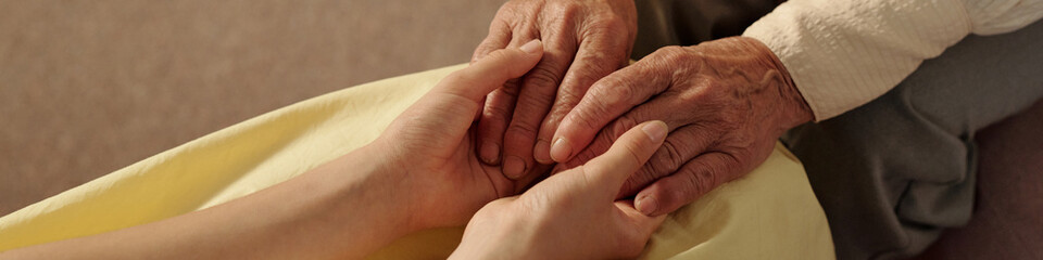 Senior Caucasian woman holding hands with young adult Caucasian woman, showing intergenerational connection and support, closeup of hands emphasizing tenderness and care
