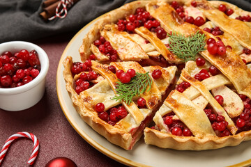 Plate with cut tasty cranberry pie and candy cane on red background, closeup. Christmas celebration