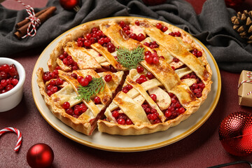 Plate with cut tasty cranberry pie and Christmas balls on red background, closeup