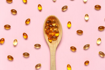 Wooden spoon with vitamin E capsules on pink background