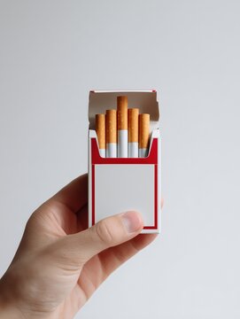 Hand holding open red cigarette pack with blank label on gray background, copy space