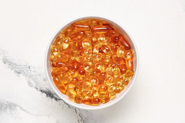 Bowl with vitamin E capsules on white background