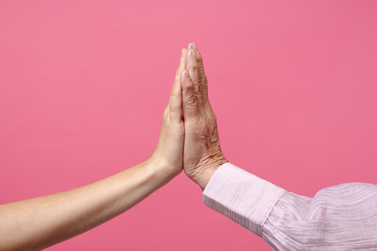 Caucasian young adult woman and Caucasian senior man giving high five, hands touching against pink background, showing generational connection and interaction, only hands visible