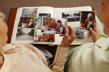 Senior Caucasian women sitting together holding photograph looking at photo album with images of...