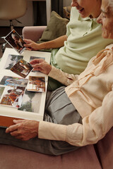 Senior Caucasian woman and middle aged Caucasian woman sitting together on sofa viewing old photographs and photo album, sharing memories and reminiscing about past moments