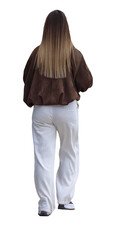 Femme vue de dos portant une veste marron ample et un pantalon large blanc, cheveux longs lisses, elle marche de manière décontractée, consultant son téléphone portable