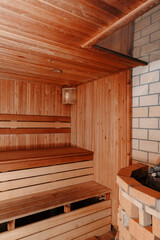 Warm cozy sauna interior with wooden walls, ceiling and floor, featuring a stove with hot stones in the corner. Soft and dim lighting creates a relaxing and intimate atmosphere.