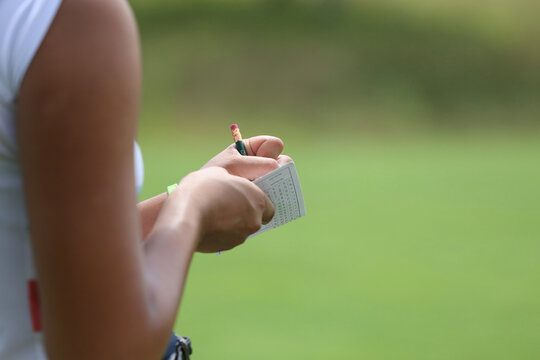 Golfer recording scores on a scorecard during a game on a sunny day