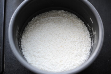White rice in a rice cooker covered in water ready for boiling as food ingredient