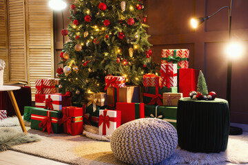 Decorated Christmas tree with many gifts and glowing lamps in living room at night