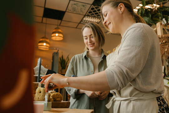 Smiling saleswoman cutting bar of soap by customer in store