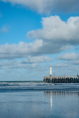 Fototapeta premium Nieuwpoort, West-Vlaanderen, Belgium, Ocotber 25th, 2025, serene coastal scene, quiet seaside pathway leading to lighthouse amidst clouds and reflections