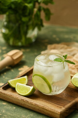 Glass of lime infused water with mint leaves on green table, closeup