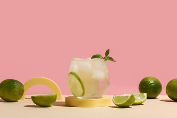 Glass of lime infused water with mint leaves on beige table against pink background