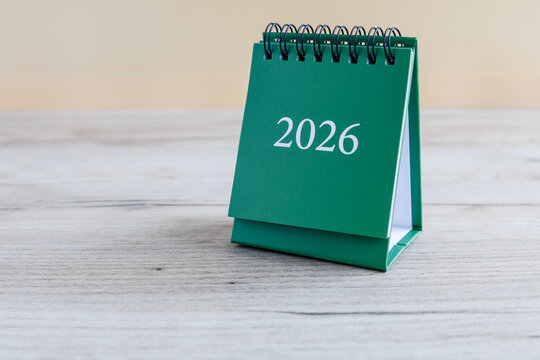 Small green desk calendar stands on wooden table, displaying year 2026. It is set up for planning future events and appointments in neat and organized manner.