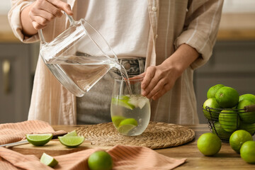 Woman pouring lime infused water from jug into glass in kitchen