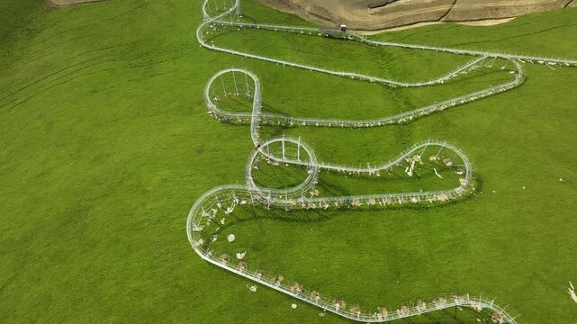 A spiraling alpine coaster twists over soft green hills, capturing a unique mix of adventure and nature within an open and sunny mountain landscape.