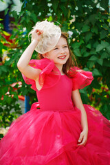 A girl in a lush pink dress and hat near the green bushes