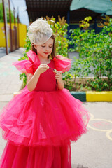 A cute little girl in a lush pink dress and hat Painting Her Lips. 
