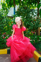 A girl in a lush pink dress and hat near the green bushes